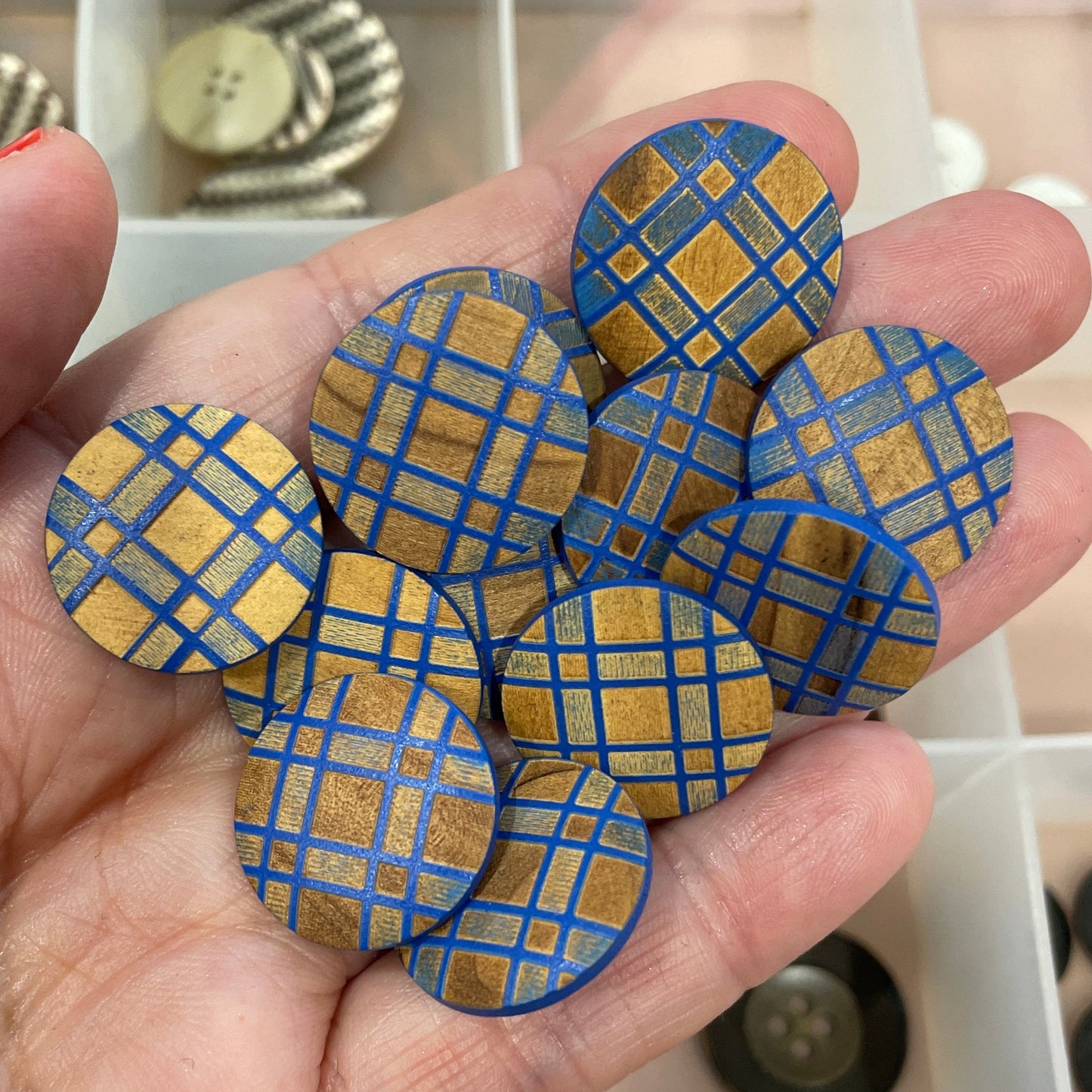 Hand holding blue and gold checkered buttons with a button organizer in the background