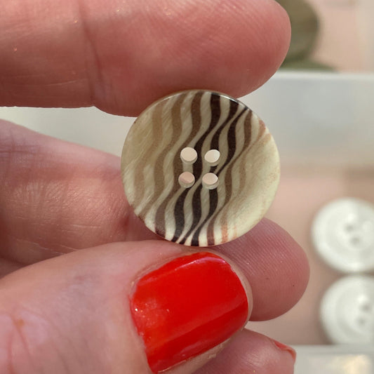 Hand holding a button with a zebra pattern against a background of various buttons.