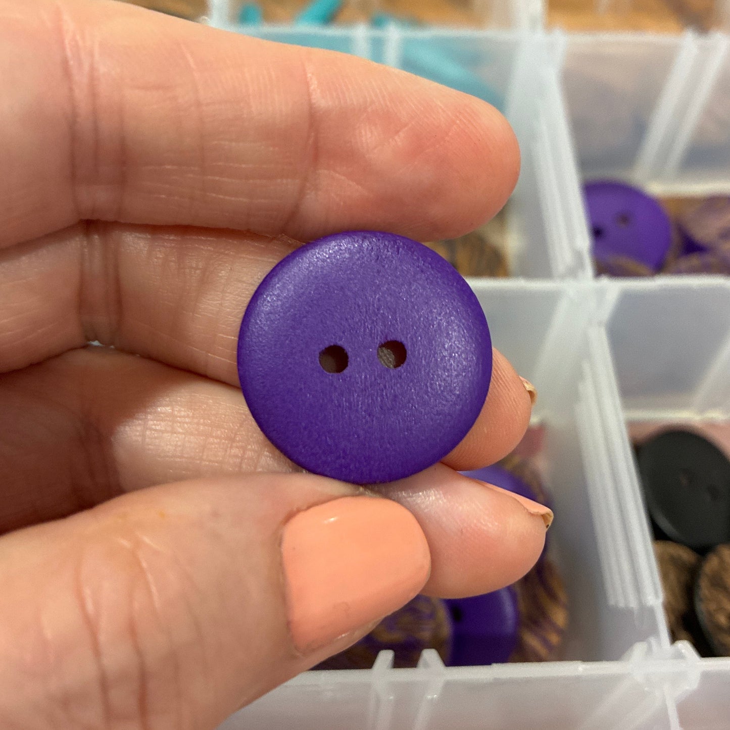 Purple button held between fingers with a container of buttons in the background