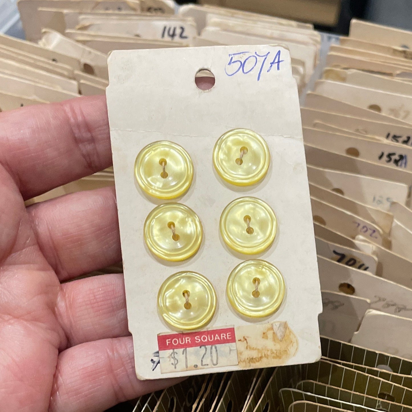 Hand holding a card with six gold buttons next to a container of similar buttons.