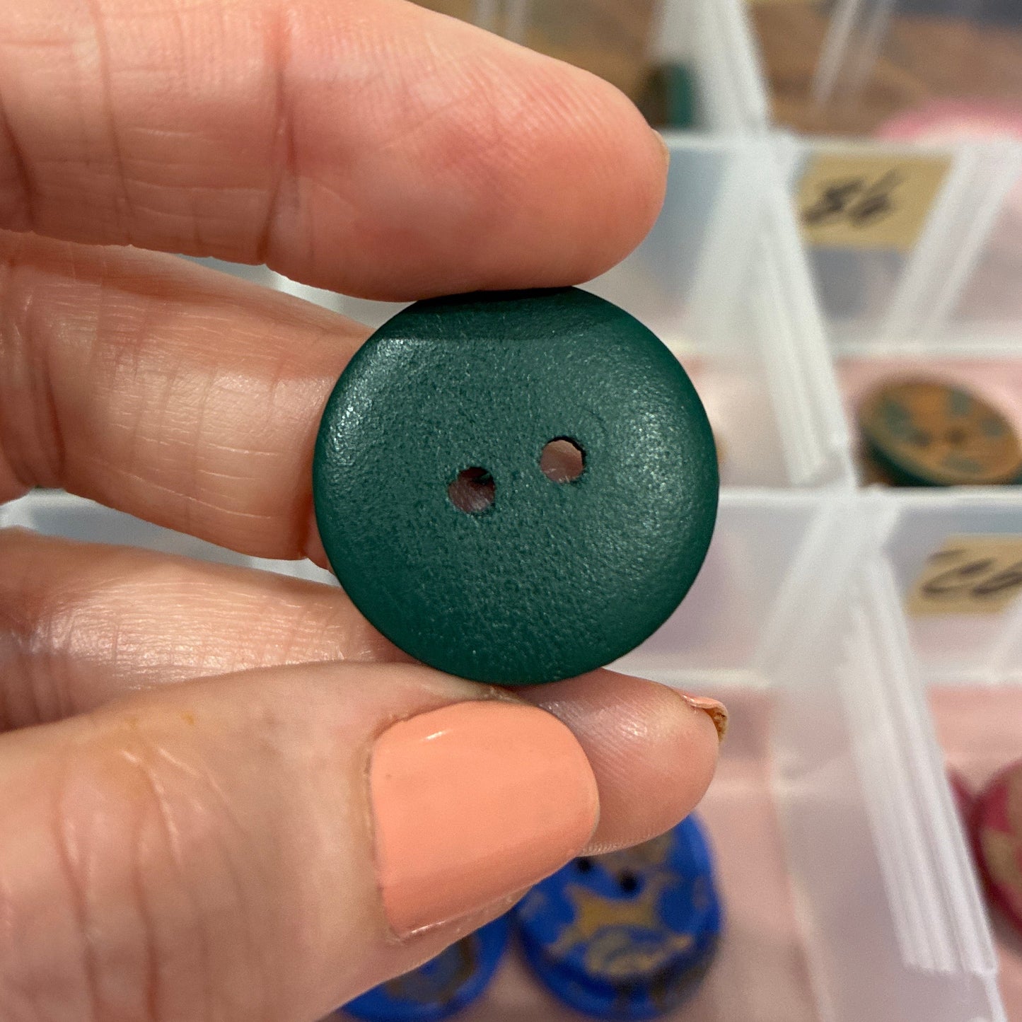 Green button held between fingers with a background of small containers.