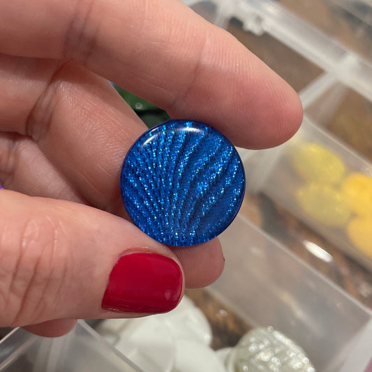 Hand holding a blue textured object with a container of various objects in the background