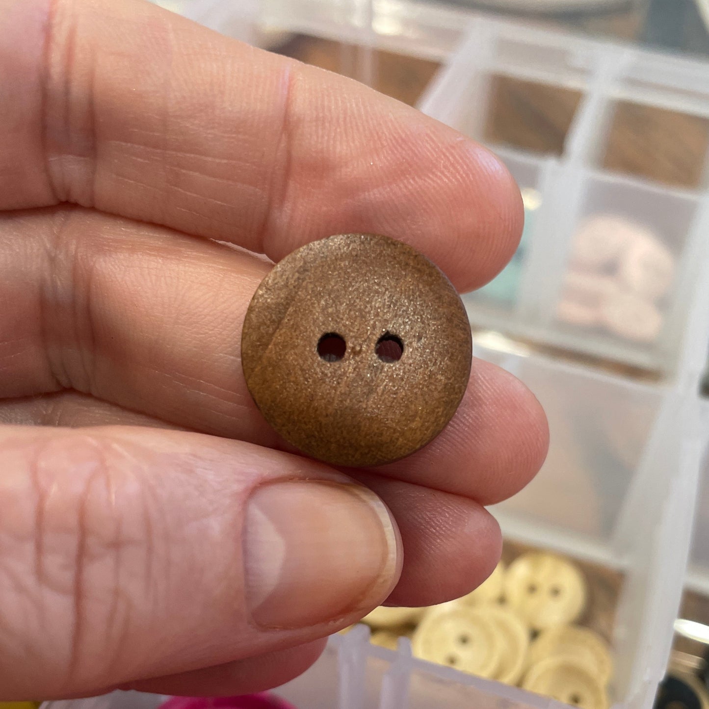 Wooden button held between fingers with pink buttons in a container in the background