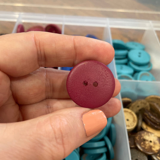 Hand holding a red button with a container of buttons in the background