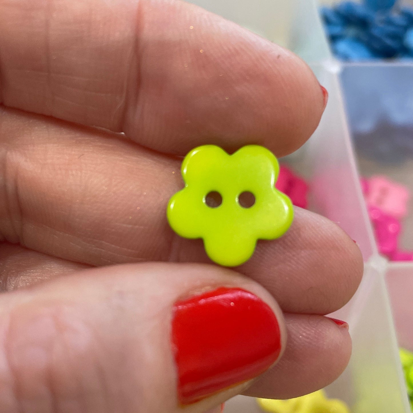 Hand holding a yellow flower-shaped button with a red nail polish, with more buttons in the background.