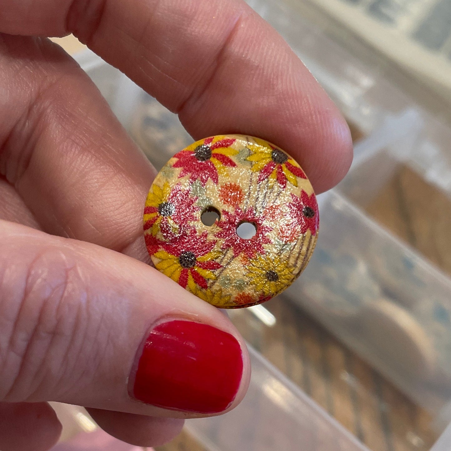 Hand holding a floral button with a container of various buttons in the background