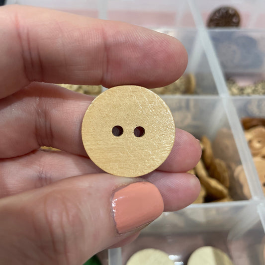 Gold button held between fingers with a container of buttons in the background