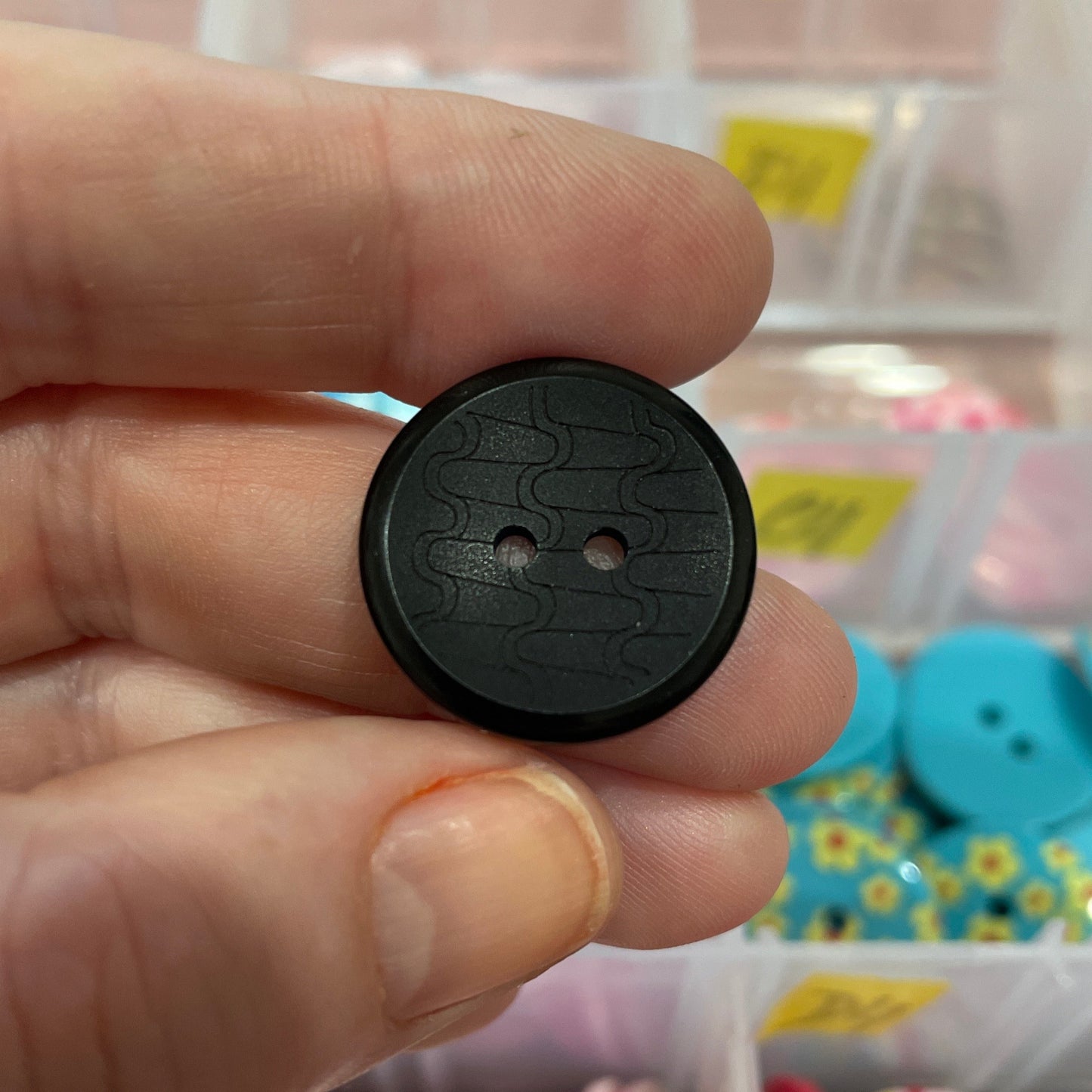 Black button held between fingers with a colorful assortment of buttons in the background