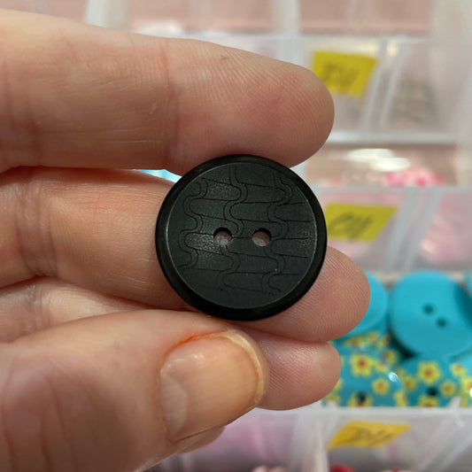 Black button held between fingers with a colorful assortment of buttons in the background