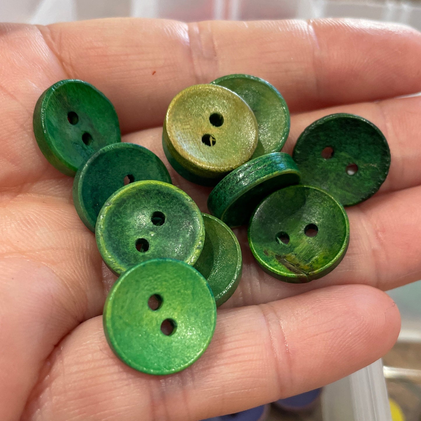 Hand holding green buttons with a container of buttons in the background