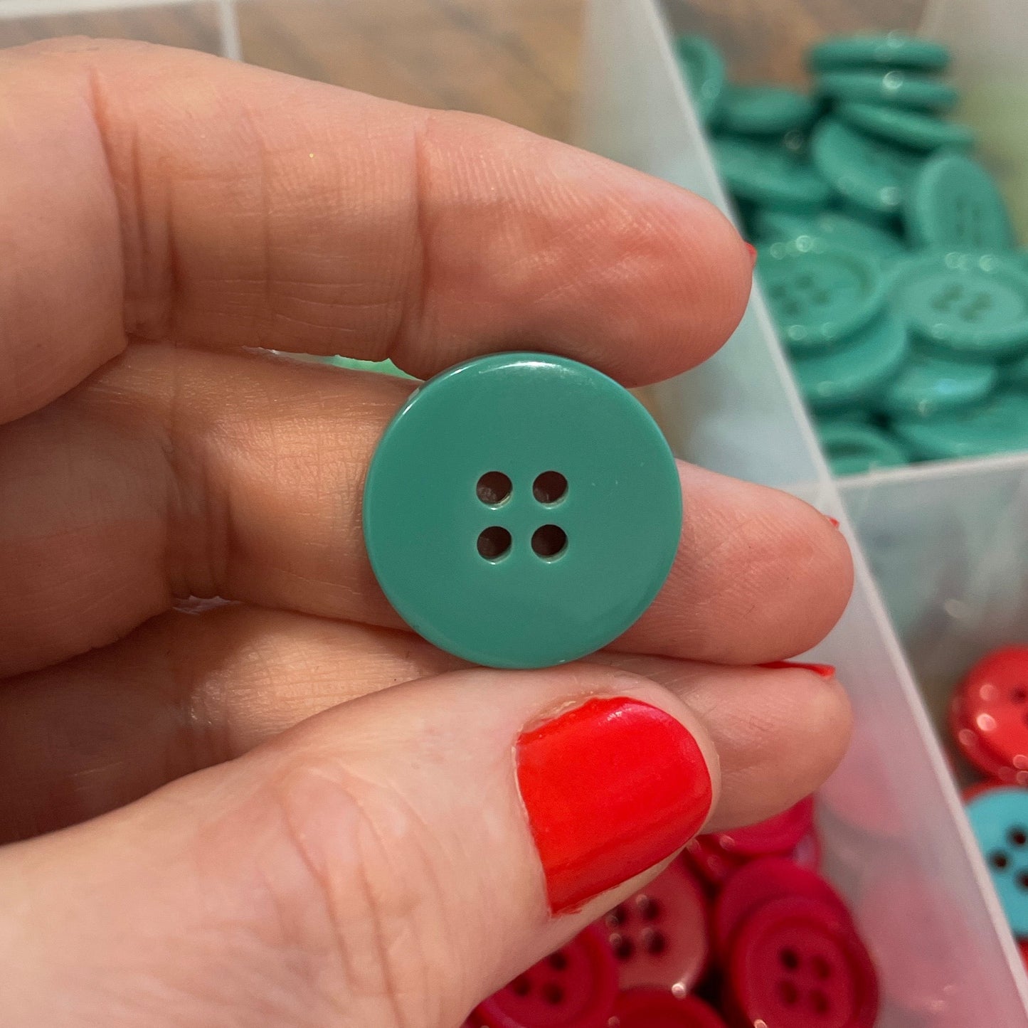 Hand holding a teal button with a clear container of colorful buttons in the background