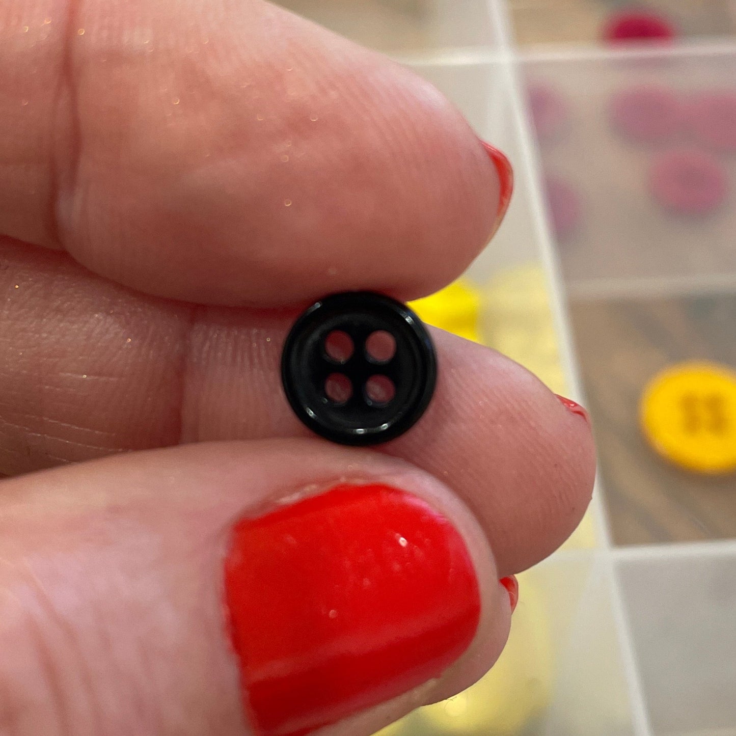 Hand holding a small black button with a clear container of colorful buttons in the background