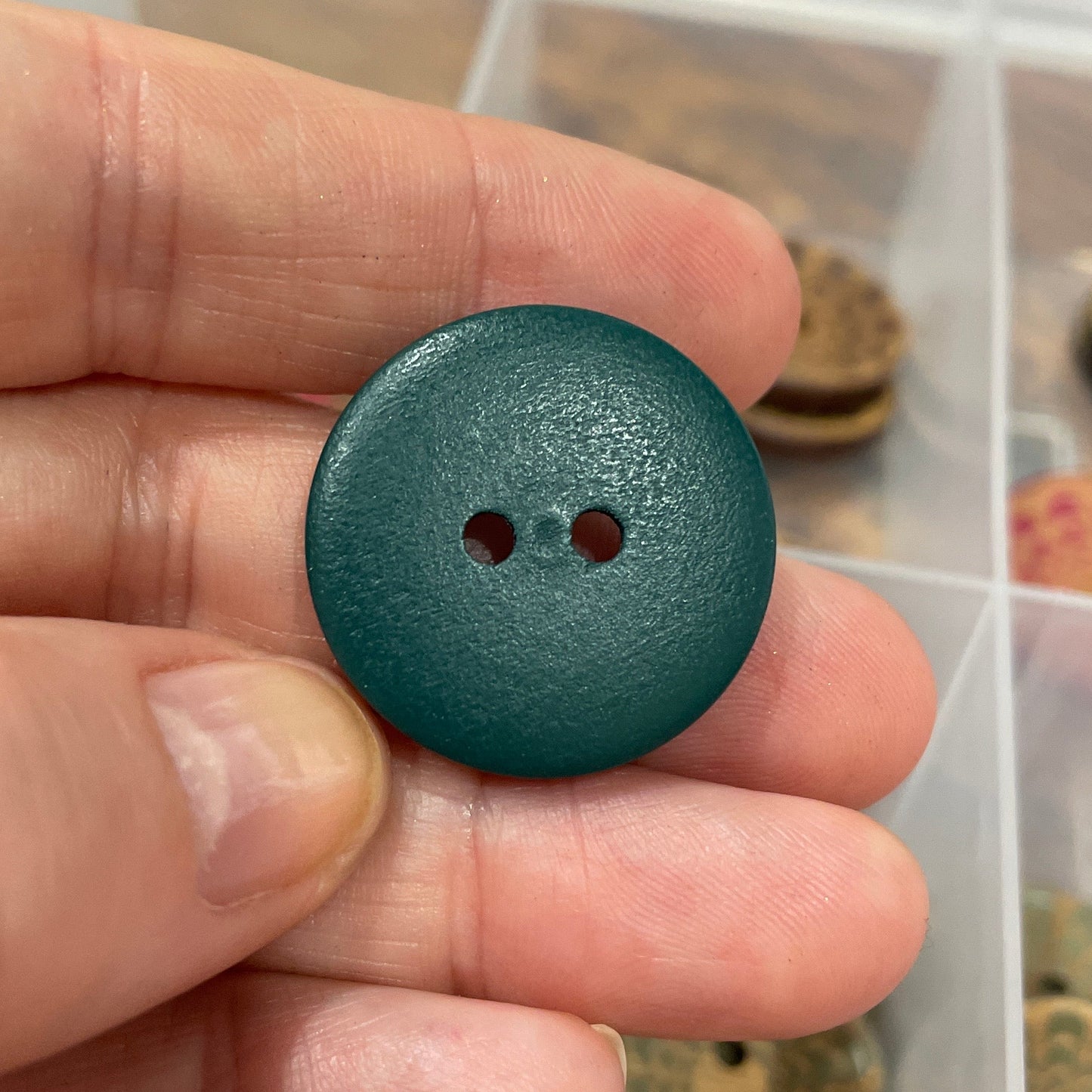Hand holding a green button with a collection of buttons in the background.