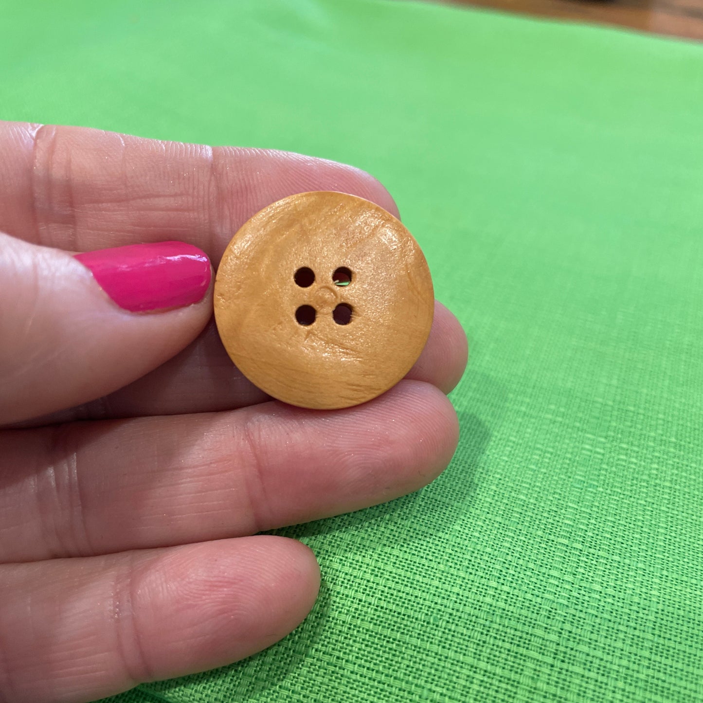 Wooden button held between fingers against a green background
