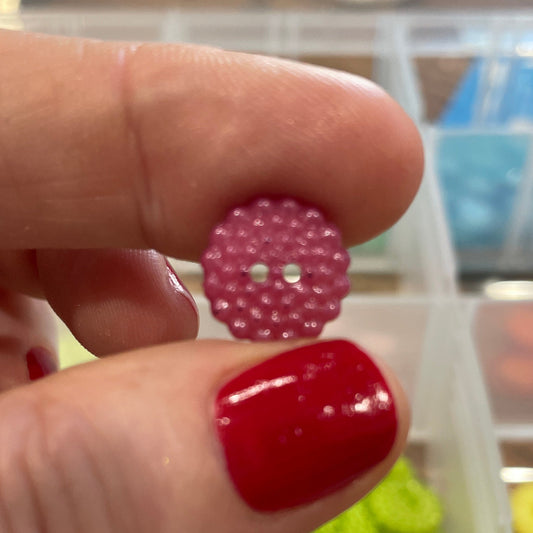 Pink button held between fingers with a container of buttons in the background