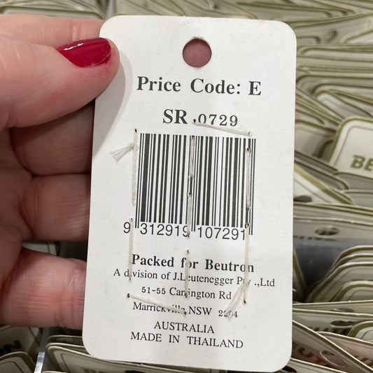 Hand holding a product tag with a barcode and text, with a blurred background of similar tags.