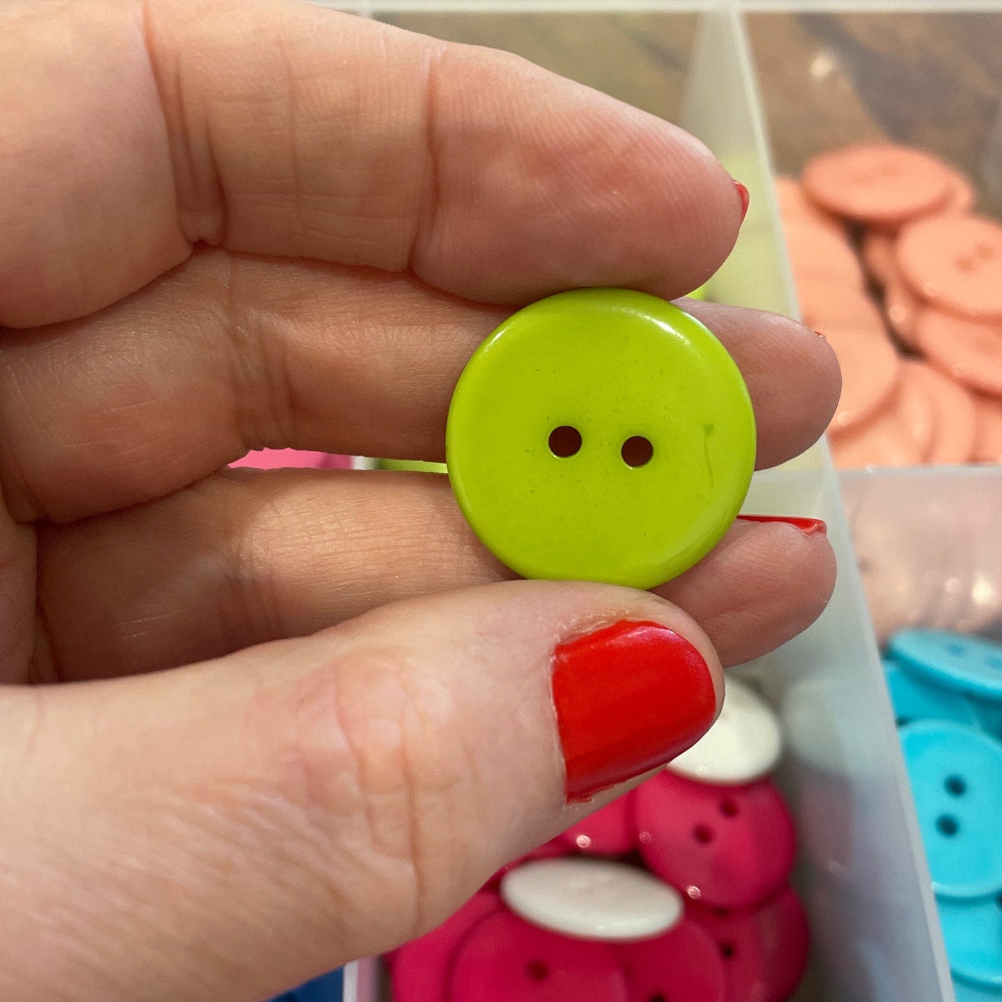 Hand holding a green button with a container of colorful buttons in the background