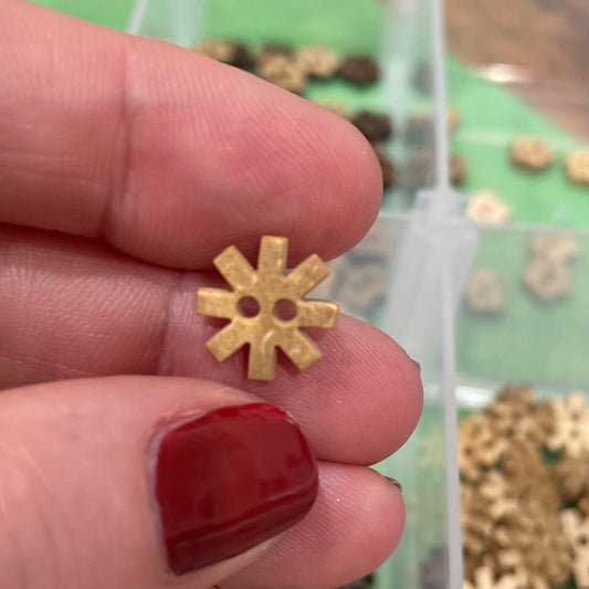 Gold snowflake-shaped button held between fingers with a container of similar buttons in the background.