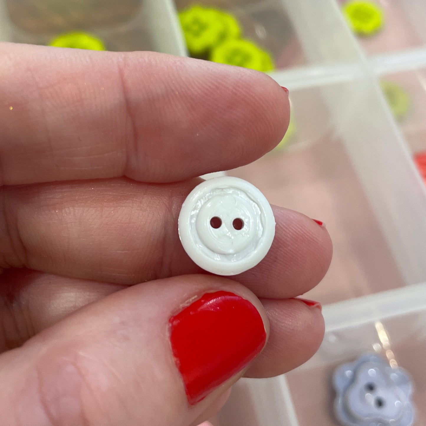 White button held between fingers with a container of buttons in the background