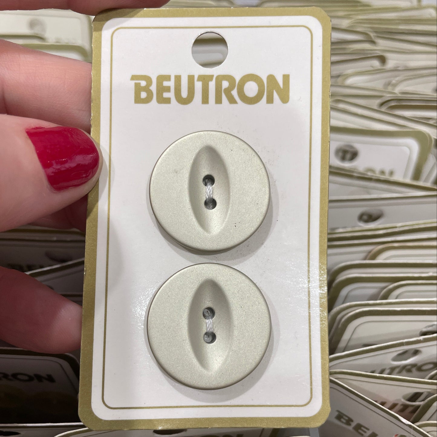 Two buttons on a Beutron branded card held by a hand with red nail polish.