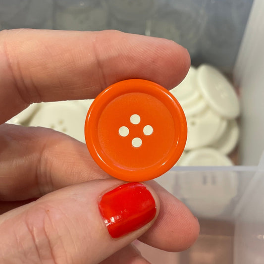 Hand holding an orange button with a clear container of buttons in the background