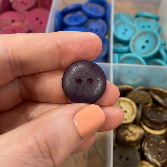 Hand holding a purple button with a container of assorted buttons in the background
