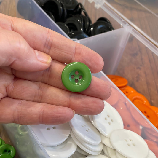 Hand holding a green button with a container of buttons in the background