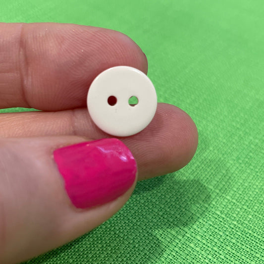 White button held between fingers against a green fabric background