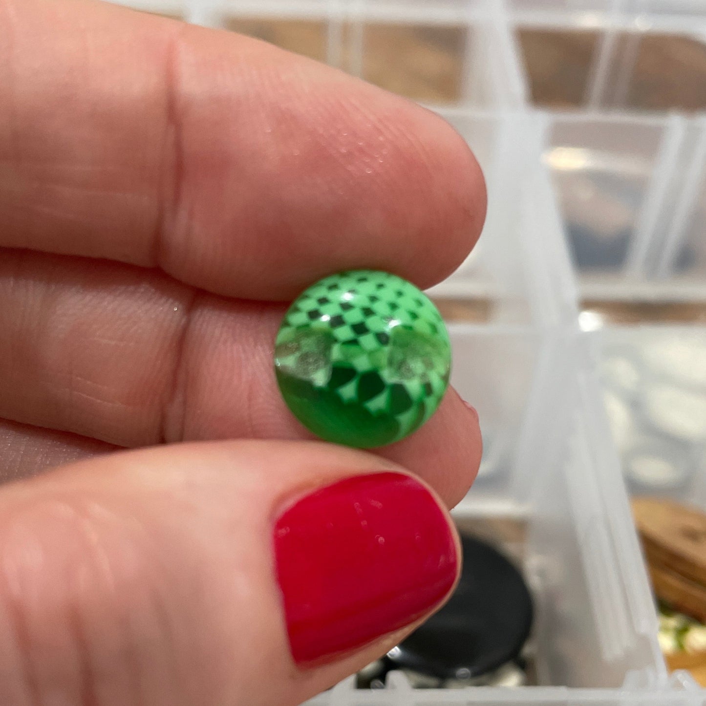 Green button held between fingers with a container of buttons in the background