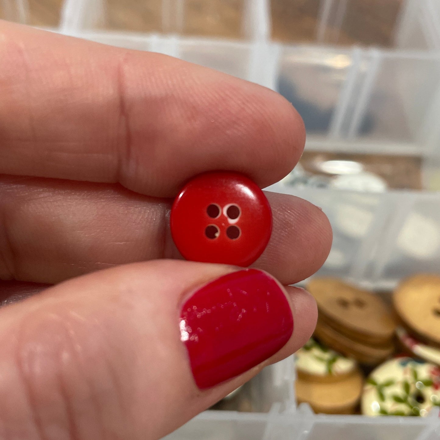 Red button held between two fingers with a container of buttons in the background