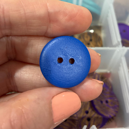 Hand holding a blue button with a blurred background of a storage box with compartments.