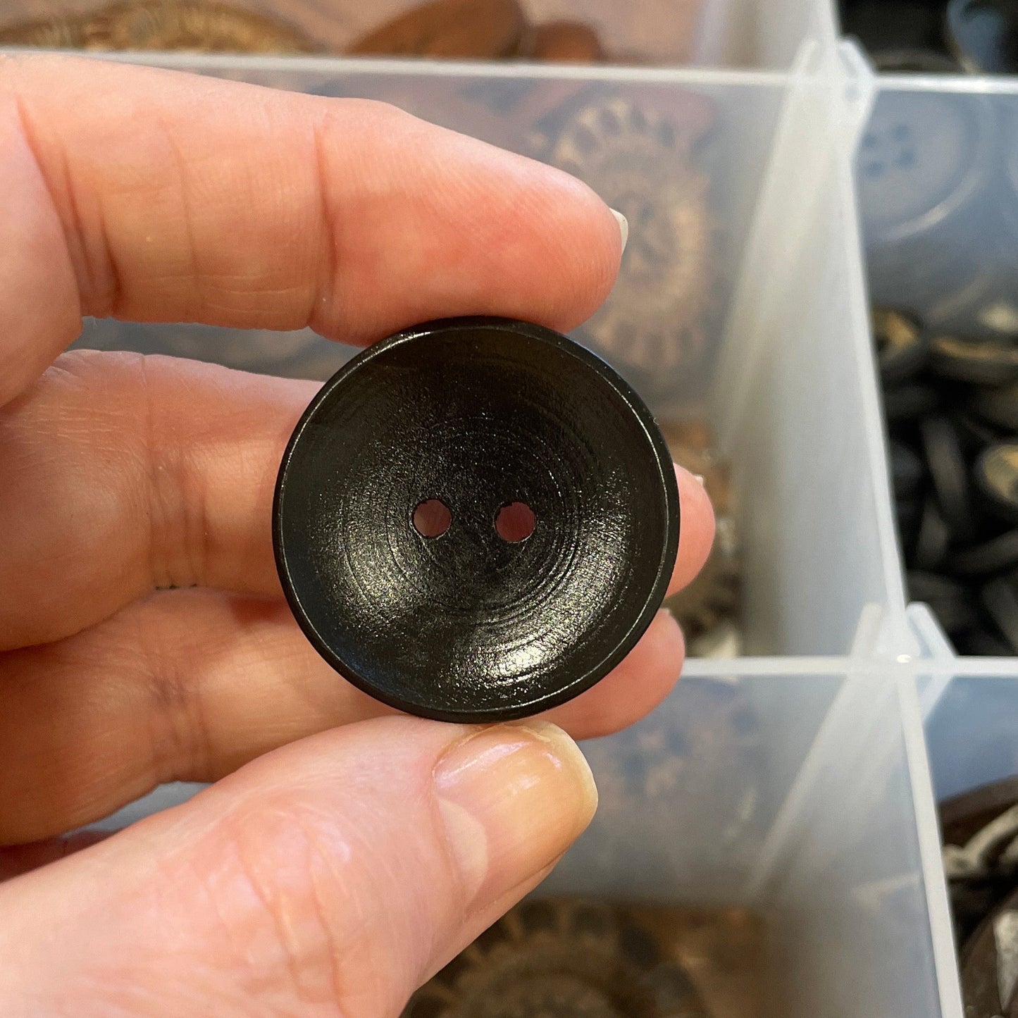 Hand holding a black button with a container of buttons in the background