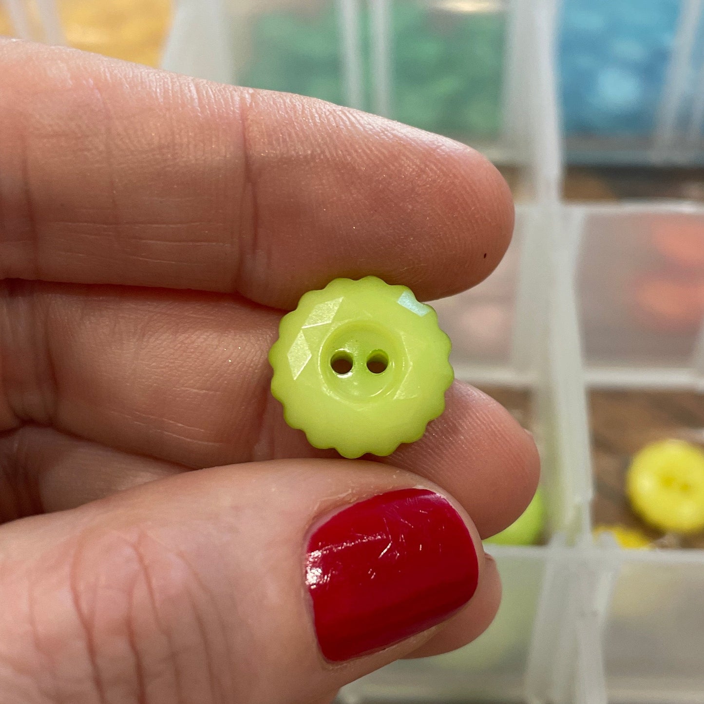 Hand holding a yellow button with a clear container of buttons in the background