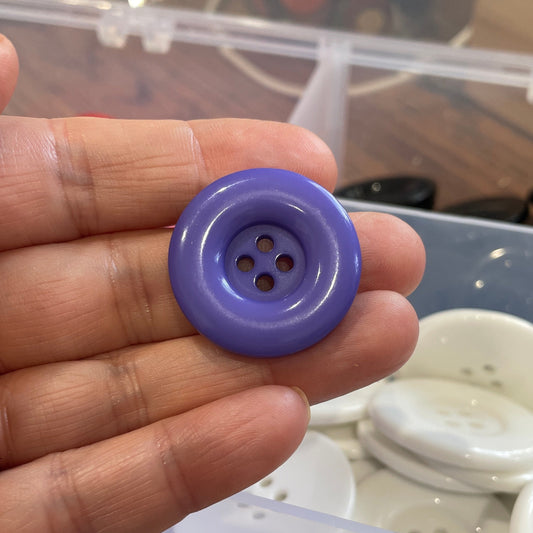Hand holding a purple button with a container of buttons in the background