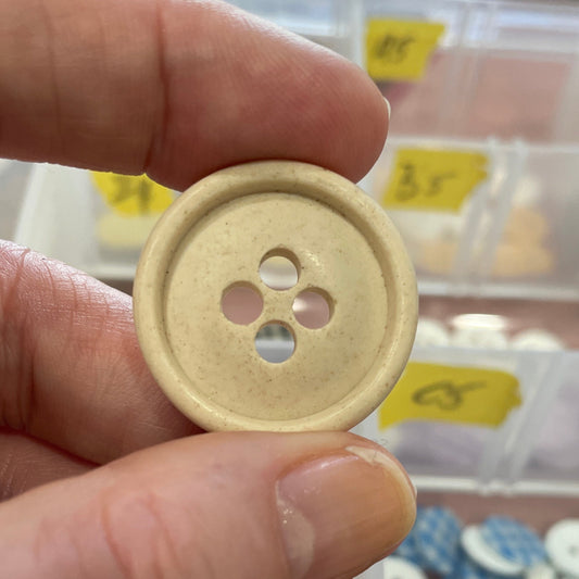 Hand holding a beige button with a blurred background of button displays.