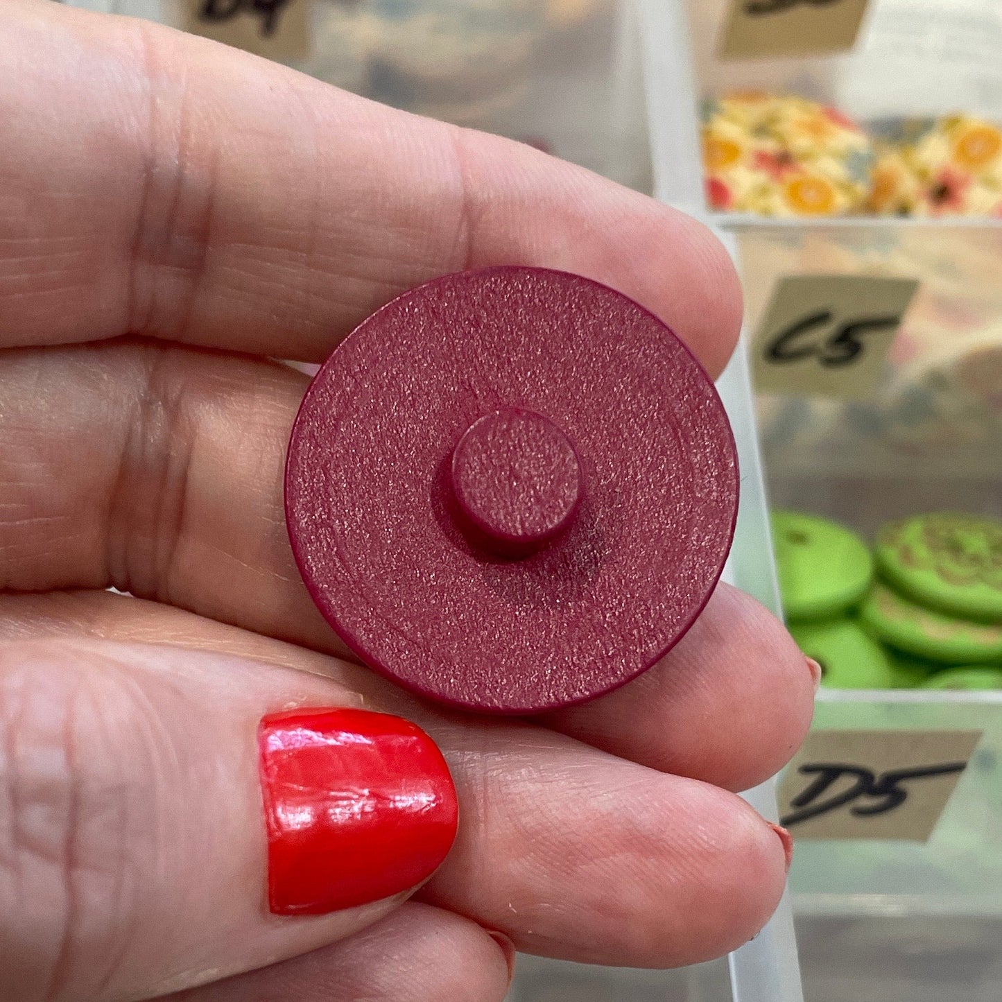 Hand holding a red button with a background of button collection in clear containers