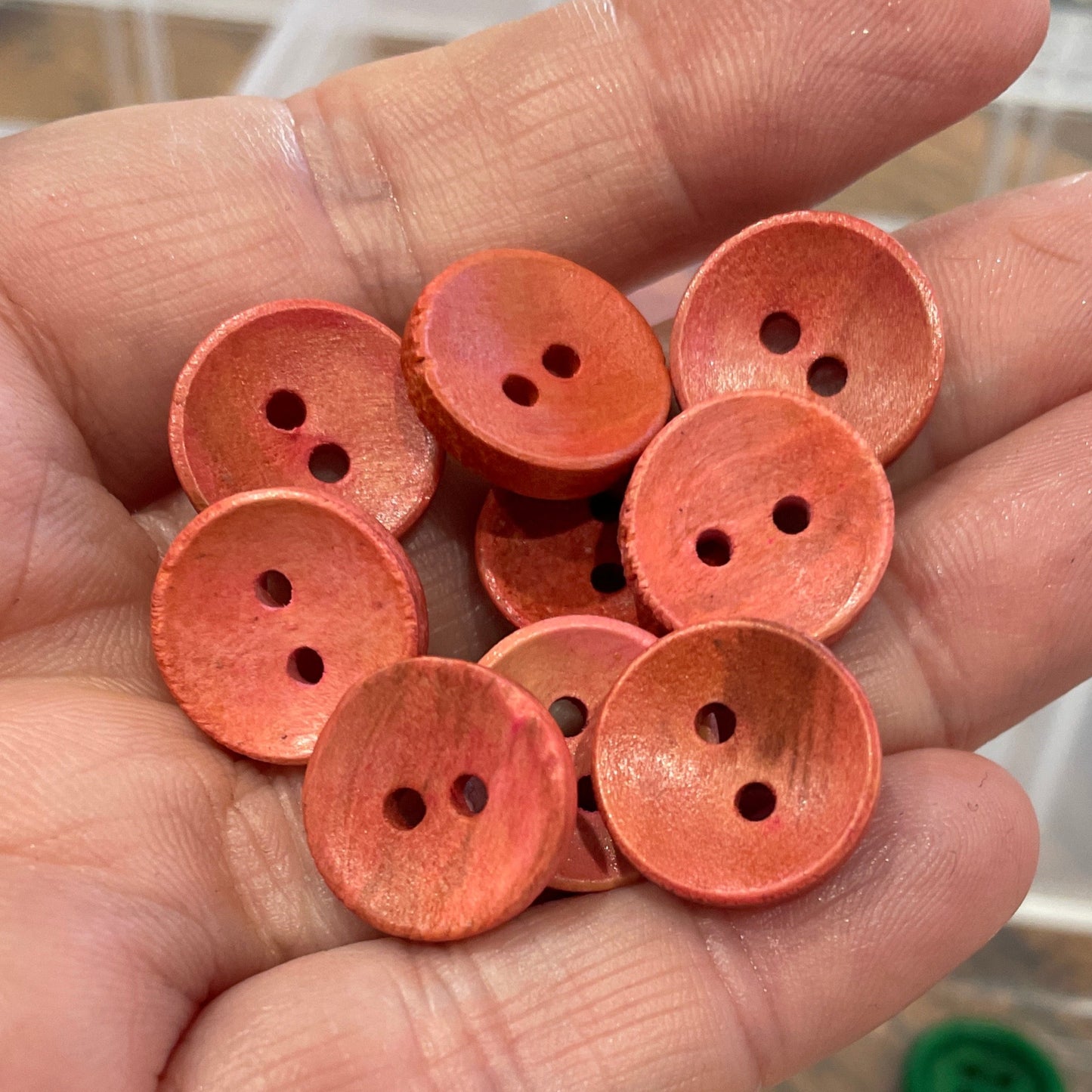 Hand holding orange buttons with a container of colorful buttons in the background