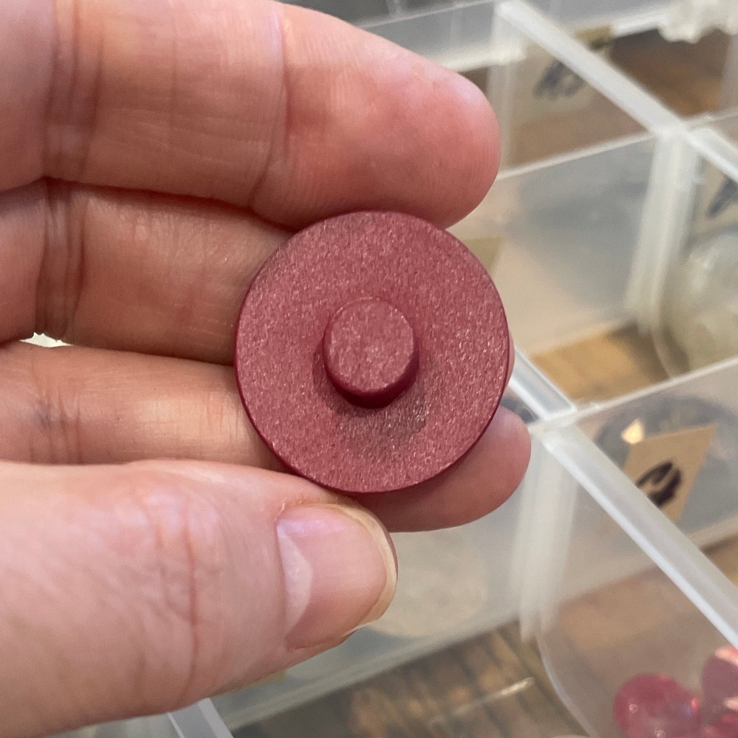 Hand holding a button with a clear container of buttons in the background