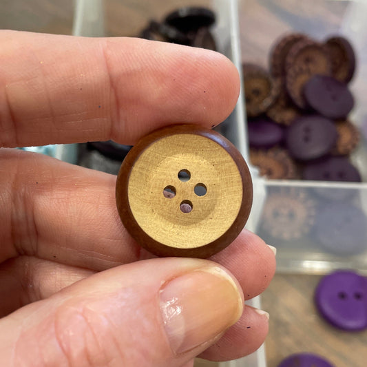 Hand holding a wooden button with a blurred background of button collection