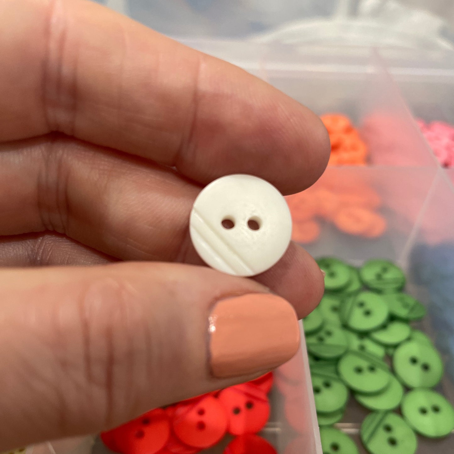 White button held by a hand with a container of colorful buttons in the background