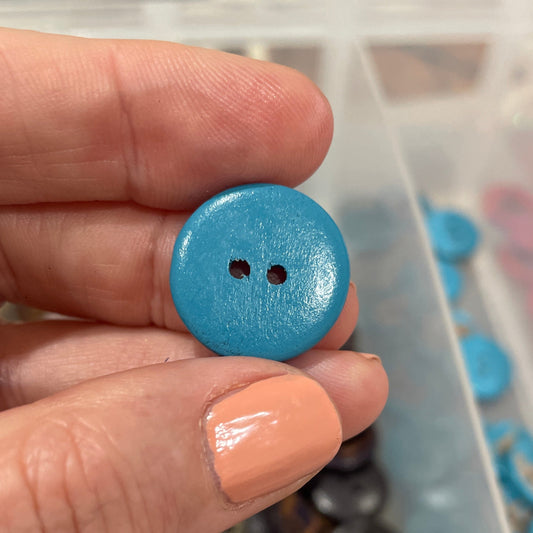 Hand holding a blue button with a clear container of buttons in the background
