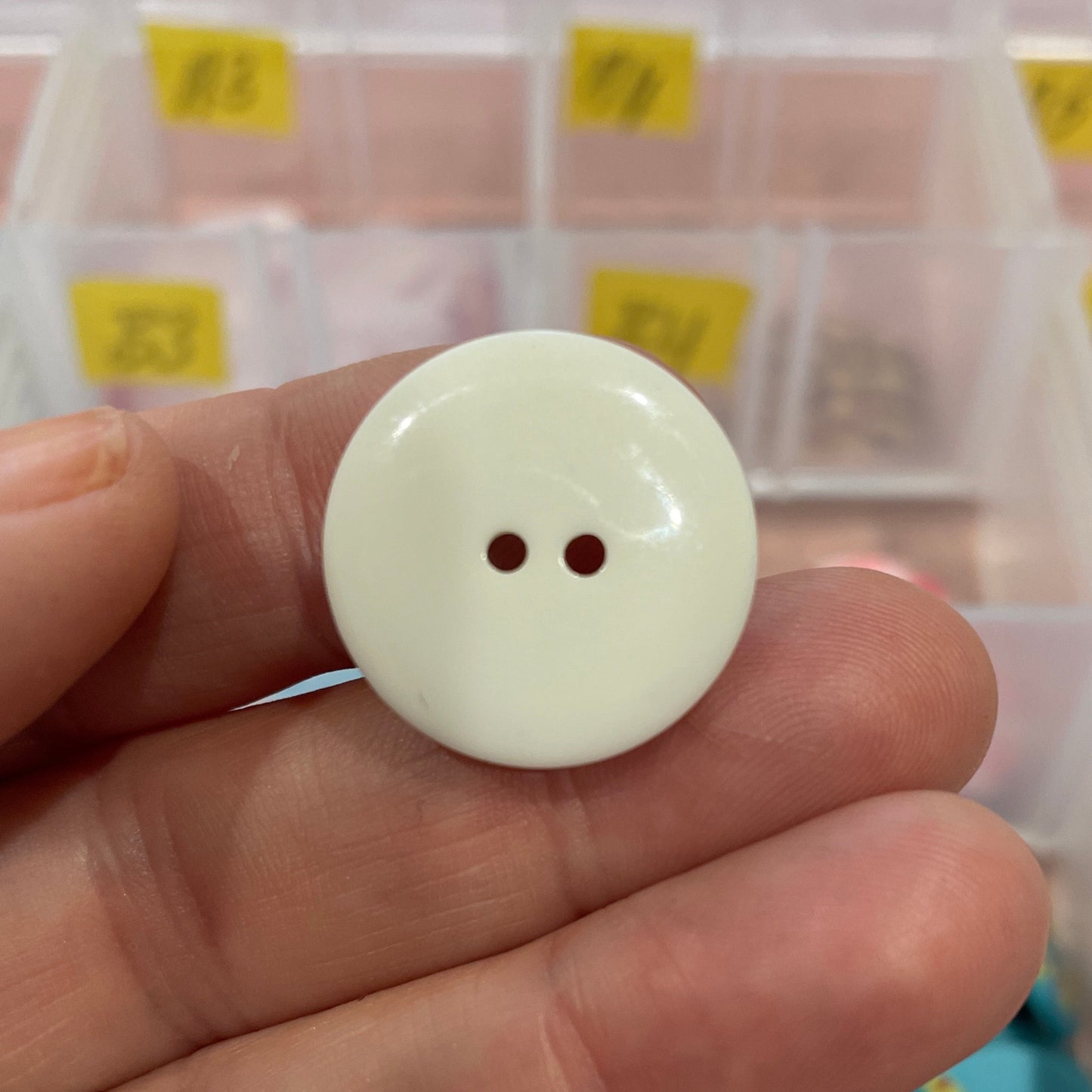 White button held between fingers with a background of colorful buttons in a container