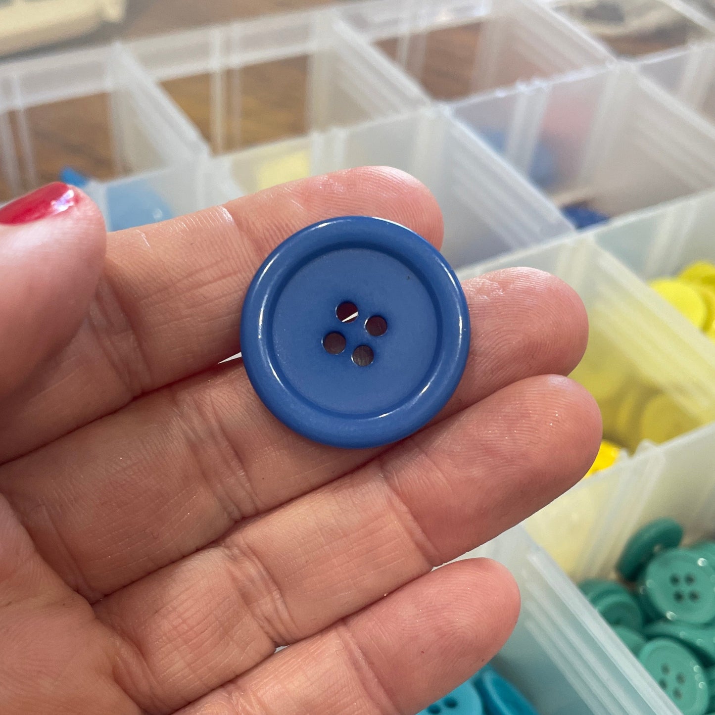 Blue button held in a hand with a container of buttons in the background