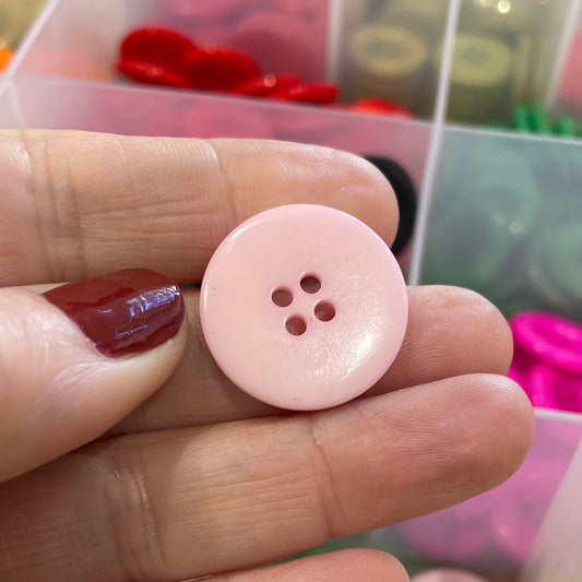 Hand holding a pink button with a container of buttons in the background