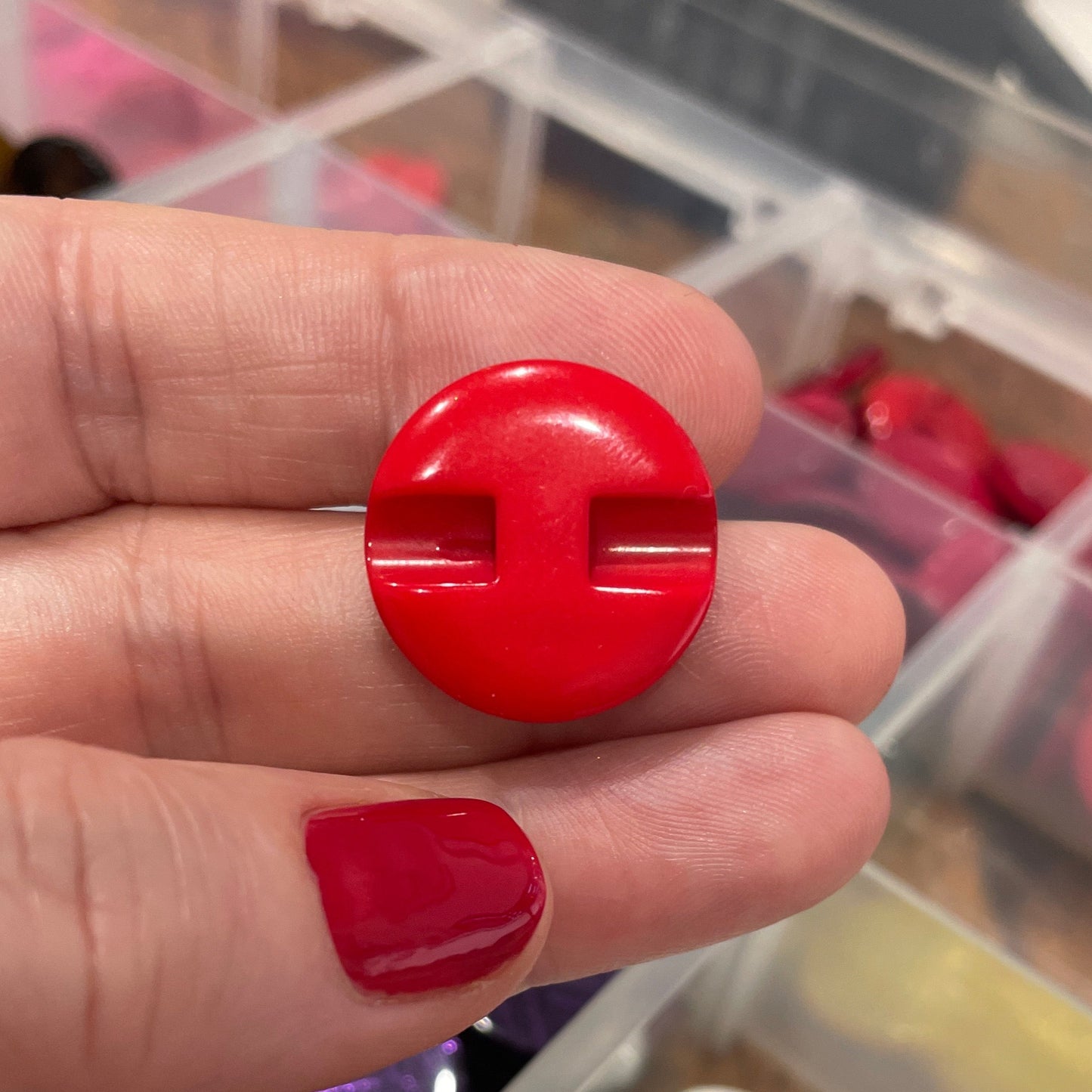 Red button between fingers, blurred container of buttons in the background