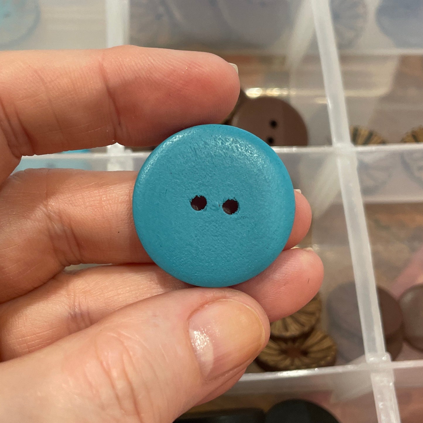 Hand holding a blue button with a clear container of buttons in the background