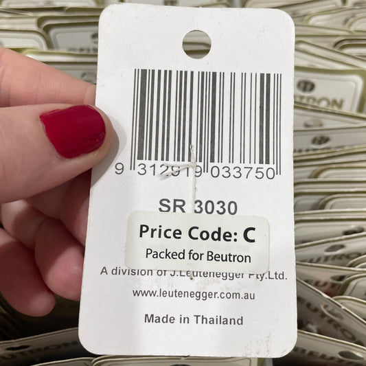 Hand holding a product tag with a barcode and text, with a background of similar tags.