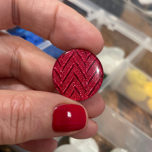 Hand holding a red textured button with a container of buttons in the background