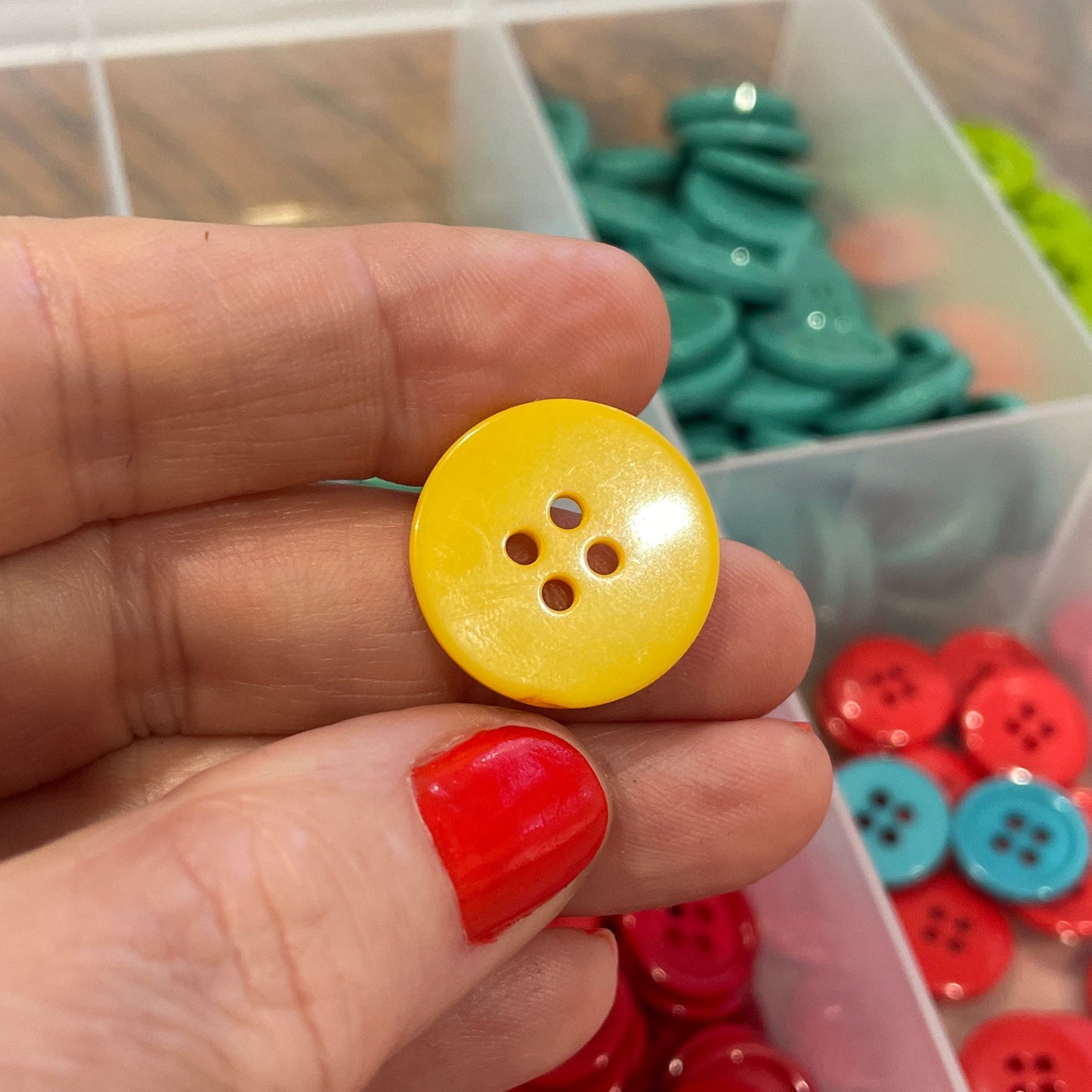 Hand holding a yellow button with a container of red buttons in the background