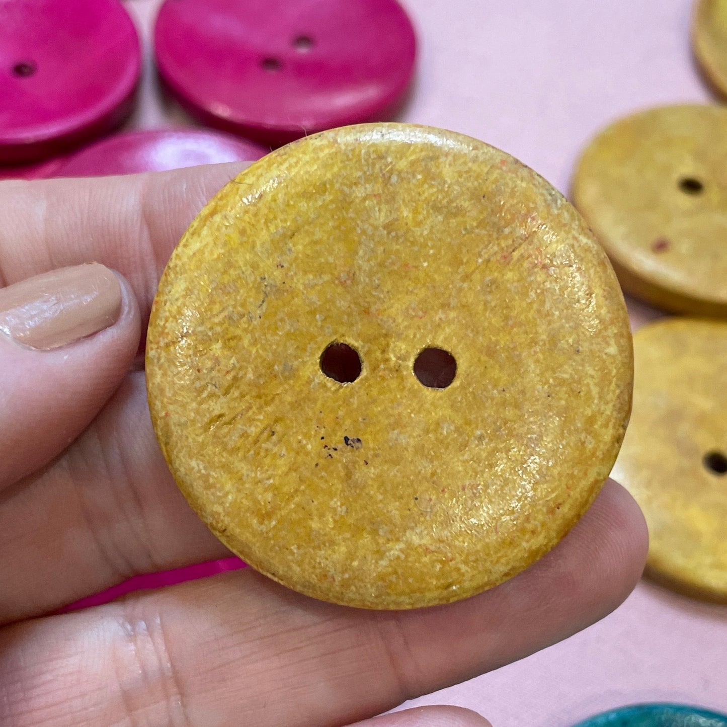 Hand holding a yellow button with colorful buttons in the background